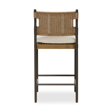 A contemporary bar stool featuring a dark-colored metal frame, a woven synthetic rattan seat and backrest, and a light-colored fabric cushion. The stool includes an integrated footrest for comfort. The backrest has cut-out handles on either side, and the overall aesthetic is clean and modern, suggesting suitability for both indoor and outdoor environments. — 3D model