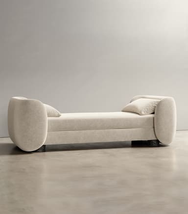 A modern daybed featuring a long, rectangular upholstered surface with two identical, generously rolled ends that serve as armrests or backrests. It is covered in a light, neutral-toned textured fabric, accompanied by a matching rectangular throw pillow. The daybed rests on a low, recessed base with small dark feet. — 3D model