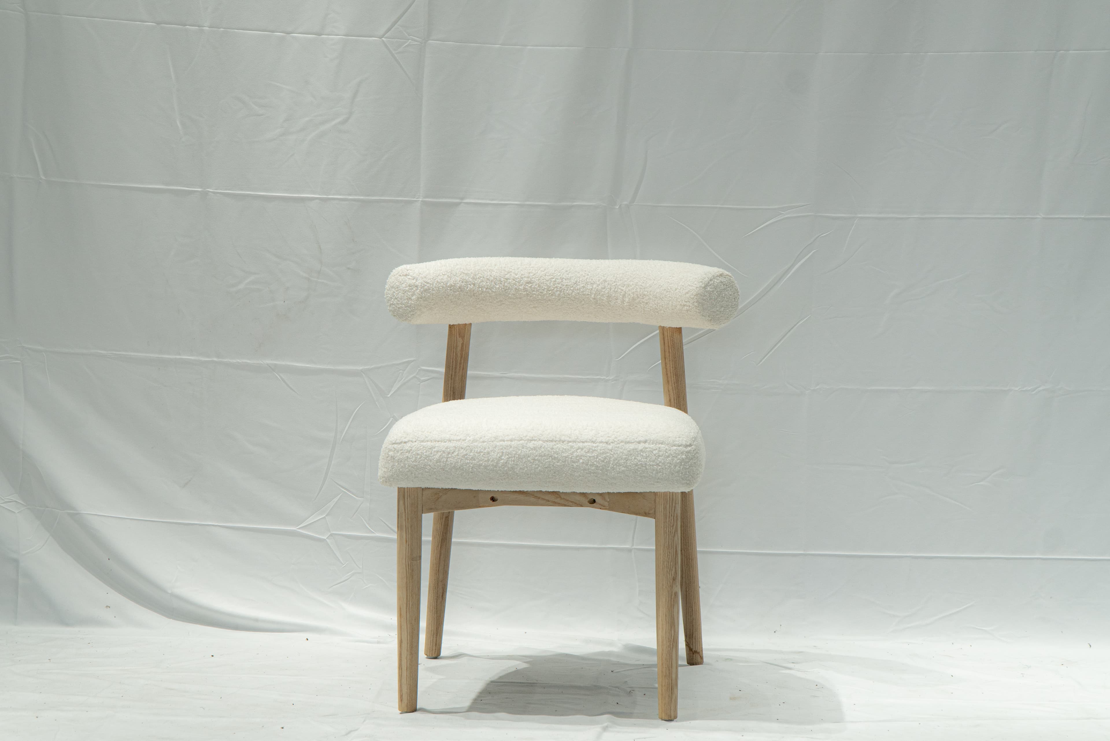 A contemporary side chair with a rounded backrest and seat upholstered in a textured, boucle fabric. The chair features a light-colored wooden frame with four tapered legs. The design is minimalist and modern. — 3D model