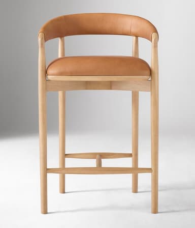 A bar stool with a curved backrest and armrests, featuring a wooden frame and leather upholstery for the seat and back. The frame consists of four cylindrical legs connected by stretchers for stability. The seat is flat and padded, while the backrest is also upholstered and curves to provide lumbar support. The armrests are integrated into the frame structure. — 3D model