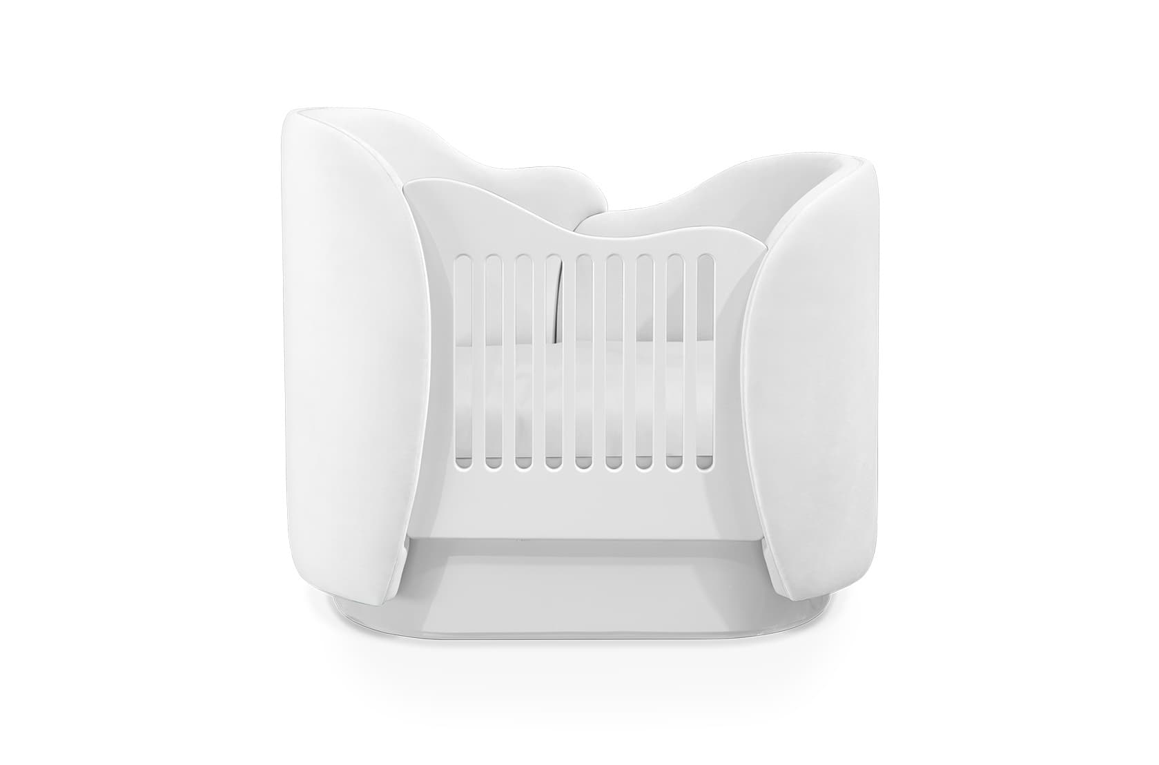 A modern, all-white infant crib featuring a distinctive oval shape and curved side panels that extend upwards and inwards, creating a cocoon-like environment. The central sleeping area is enclosed by vertical slats, likely for safety and visibility, and the crib rests on a low, subtly raised base. The clean lines and uniform white finish suggest a contemporary design aesthetic, suitable for a minimalist nursery. — 3D model