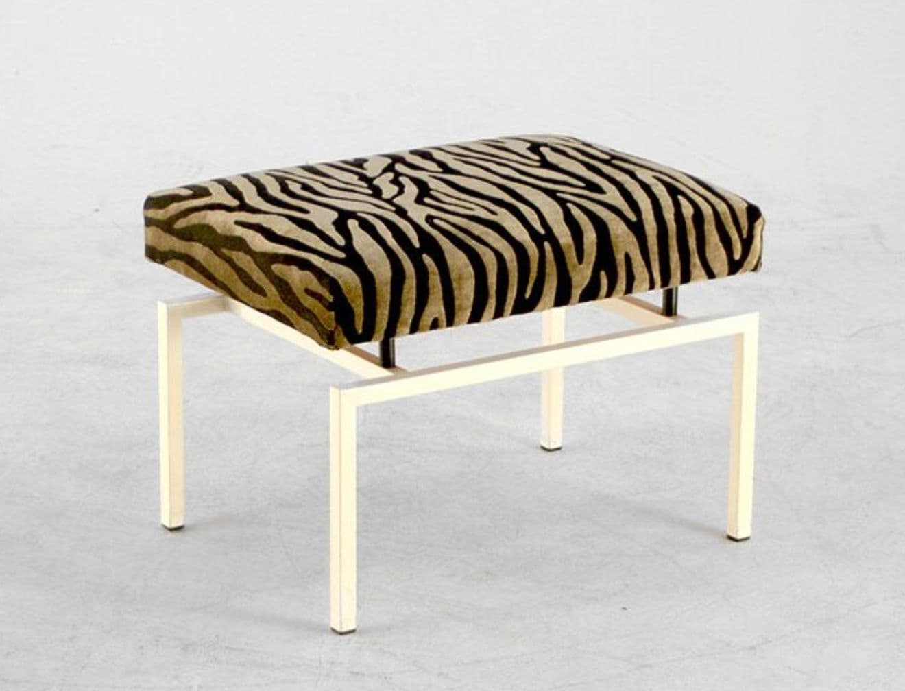 A rectangular ottoman with a metallic base and a upholstered seat. The seat is covered in fabric with a zebra print pattern. The base consists of four legs connected by a rectangular frame, creating a minimalist aesthetic. — 3D model