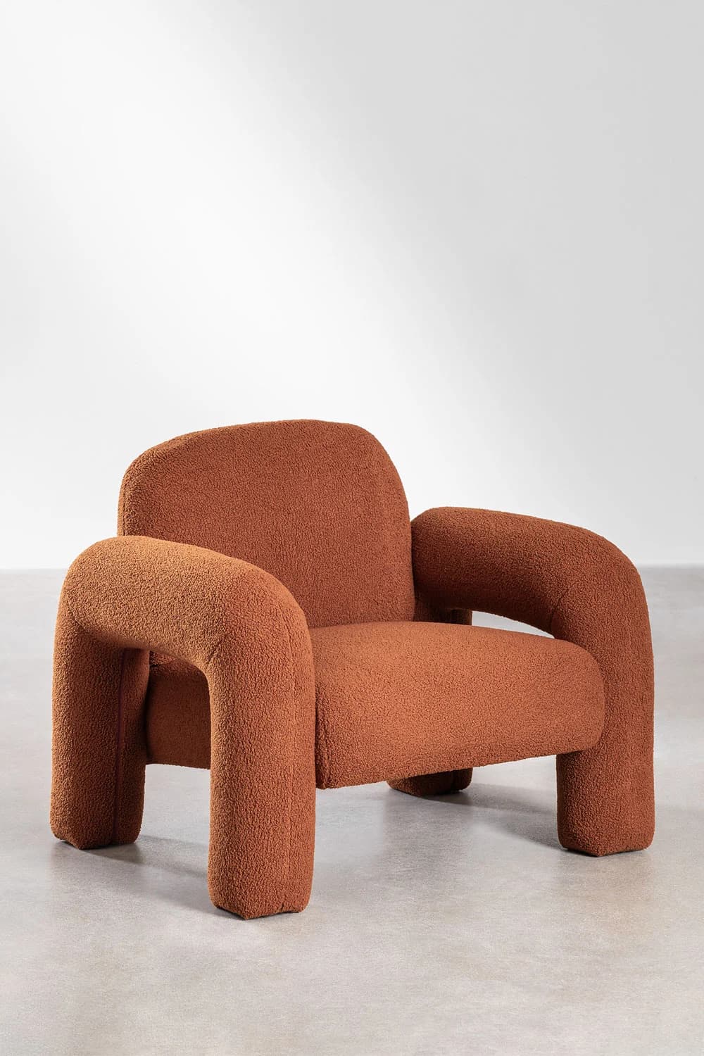 A contemporary armchair upholstered in a textured, burnt orange fabric. The chair features a distinctive design with rounded, tubular arms and legs that curve outwards. The backrest is high and also rounded, providing a comfortable seating experience. The overall aesthetic is sculptural and inviting. — 3D model