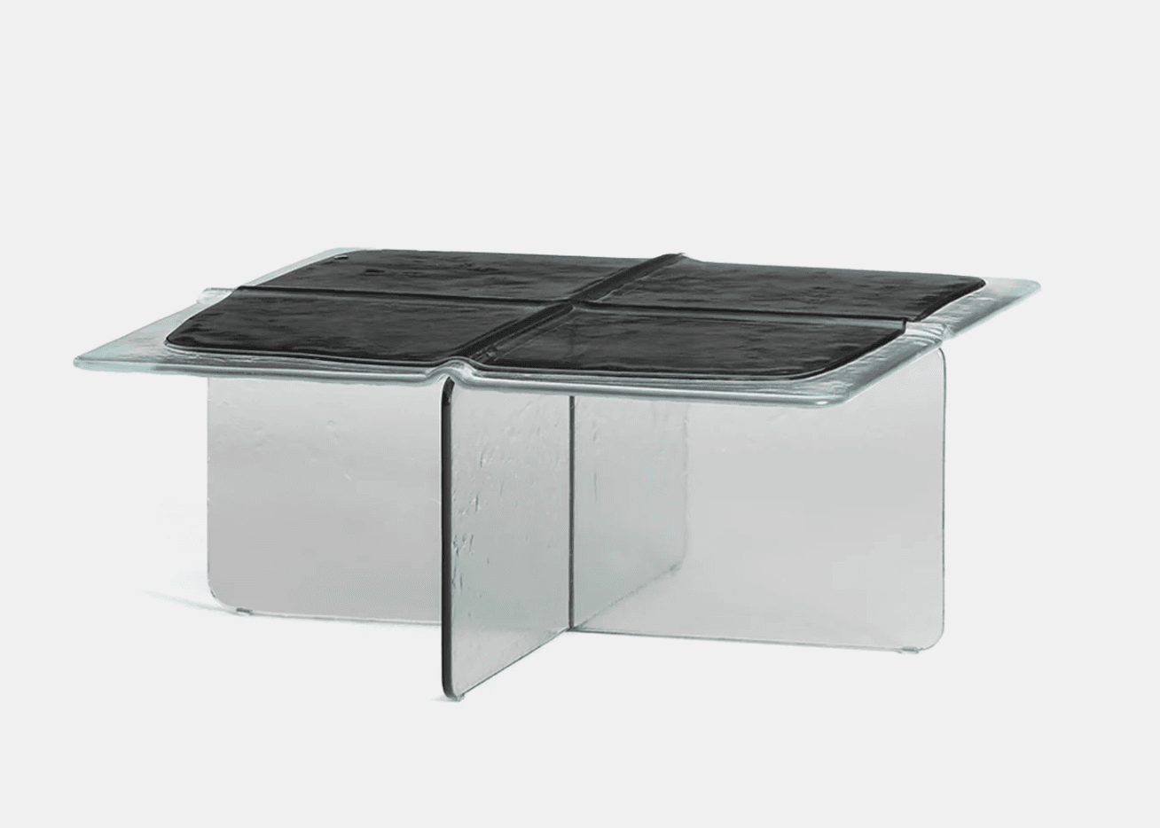 A contemporary coffee table constructed primarily from thick, clear glass. The design features a square tabletop with gently rounded edges and a central recessed area containing four distinct, textured black panels, possibly a form of faux leather or polymer. The base is formed by two intersecting glass panels, creating a stable cross-shaped support structure. The overall aesthetic is minimalist and sculptural, highlighting the material properties of glass and the contrast with the dark, textured surface. — 3D model
