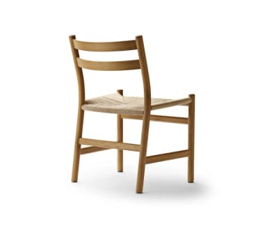 A minimalist dining chair crafted from natural oak wood, featuring an armless design with a gently curved, two-slat ladder backrest. The seat is hand-woven with natural paper cord, creating a textural contrast with the smooth wood frame. The chair stands on four round, tapered legs, with stretchers providing stability. — 3D model