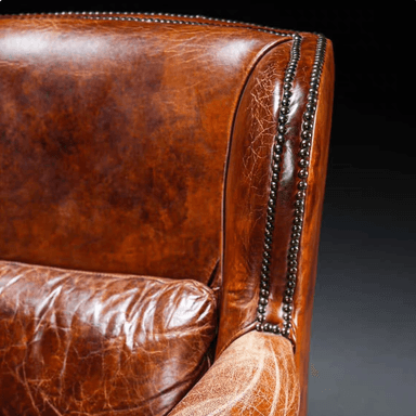 A traditional wingback armchair upholstered in rich, distressed brown leather, featuring prominent wingback sides, rolled arms, and extensive nailhead trim. It includes a loose seat cushion and a loose back cushion, supported by dark turned wooden bun feet. — 3D model