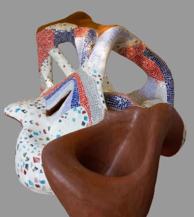 A highly sculptural, organic, and irregularly shaped seating object, primarily covered in a multi-colored terrazzo-style mosaic, with sections featuring finer, patterned mosaic tiles in red, blue, and light purple. The structure includes various openings and undulating surfaces. — 3D model