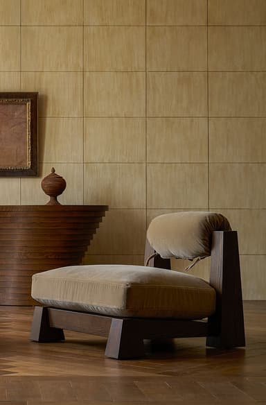 A modern armchair with a robust wooden frame and plush, upholstered cushions. The frame has a dark wood finish and features thick, geometric legs and uprights. The seat cushion is large and rectangular, while the backrest is supported by two wooden uprights and has a separate, cylindrical bolster cushion. A tie strap is visible connecting the bolster to the frame. The overall design suggests a minimalist yet comfortable aesthetic. — 3D model