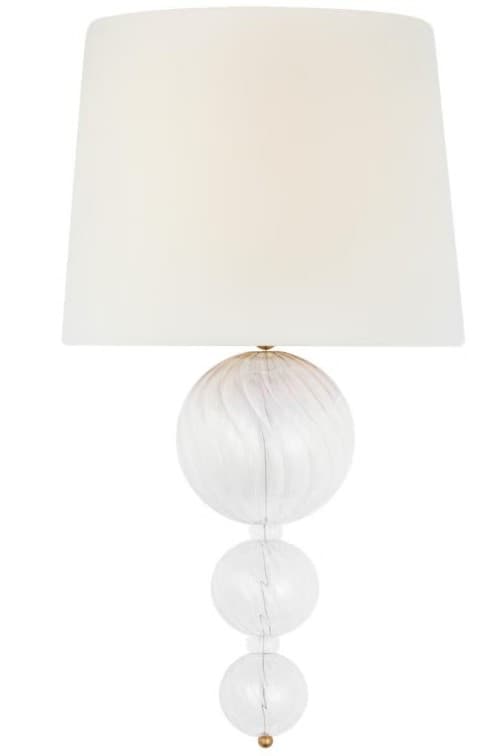 A contemporary table lamp featuring a stacked glass orb base and a white tapered fabric shade. The largest glass orb exhibits a subtle swirled pattern, adding a textural element to the otherwise clear glass components. Small brass-finished metal accents are visible between the glass sections and at the very top, connecting to the shade. — 3D model