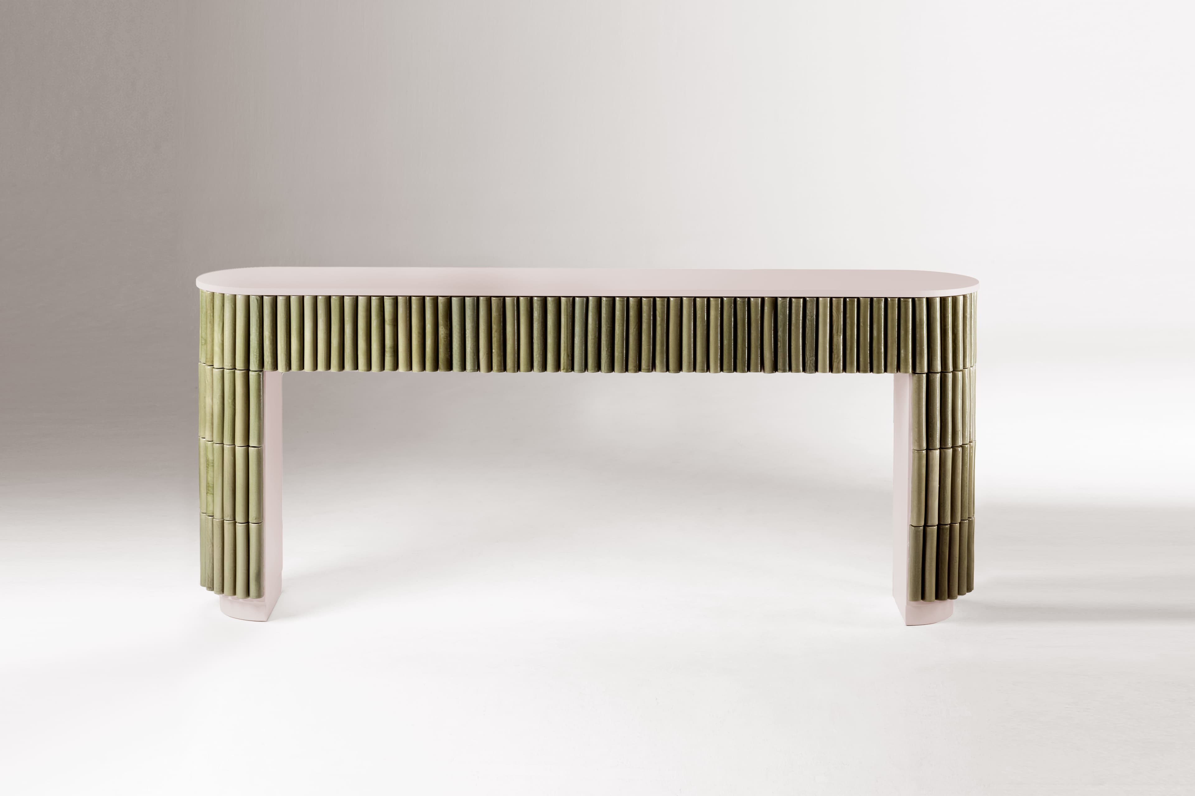 An elongated, narrow console table featuring a light pinkish-beige top and structural elements. The front and sides are extensively clad with vertical, muted green cylindrical elements, likely ceramic rods, creating a fluted or reeded texture. The base of the table follows the same pinkish-beige tone and features a subtle arched shape. — 3D model