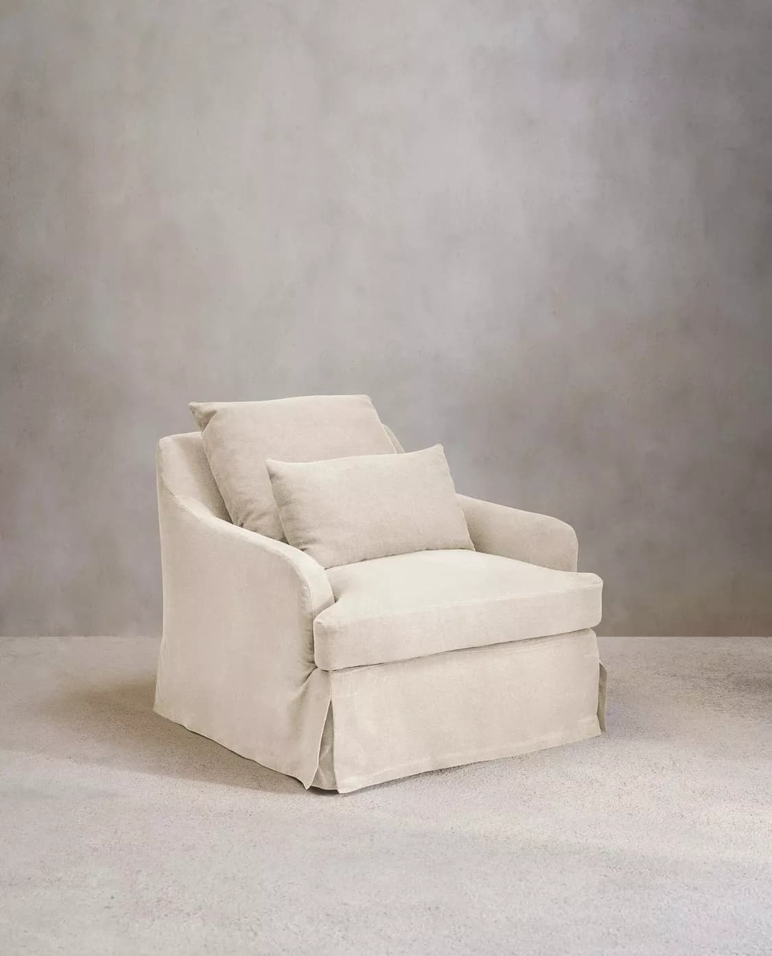 A slipcovered armchair with a plush, inviting appearance. The armchair features a skirted base and two accent pillows, one square and one rectangular, placed on the seat and backrest. The fabric appears to be a textured linen or cotton blend. — 3D model