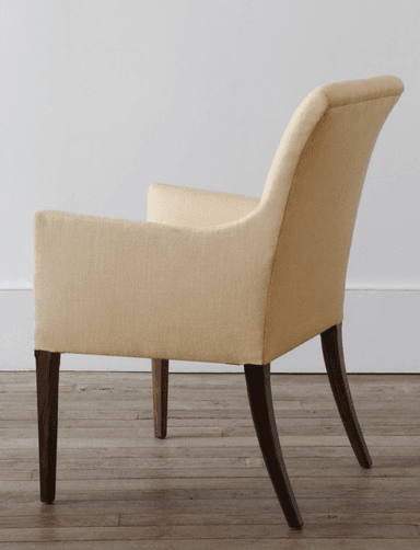 A fabric-upholstered armchair with a gently curved backrest and integrated armrests. The chair features four dark wooden legs, with the rear legs exhibiting a slight curve. The upholstery appears to be a textured woven fabric. — 3D model