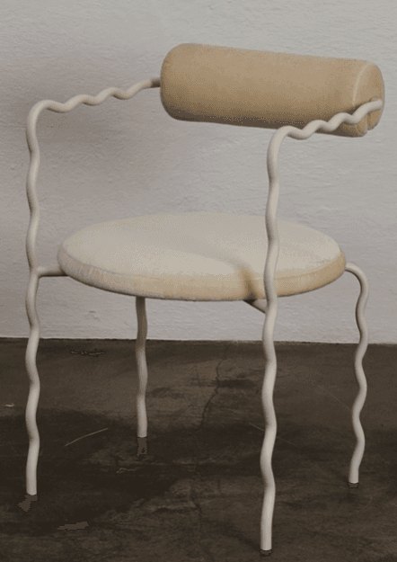 A contemporary chair with a distinctive design. The chair features a tubular, cream-colored frame with wavy, sinuous legs and armrests. The seat and backrest are upholstered in a textured, light beige fabric, with the backrest having a cylindrical pillow-like form. — 3D model