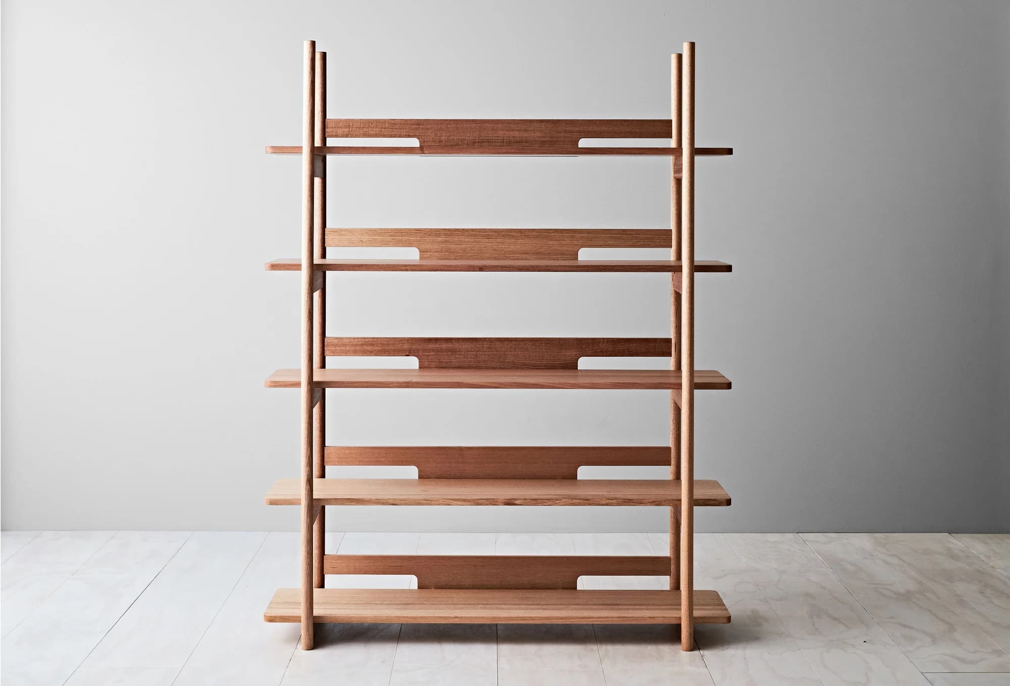 A wooden bookshelf with a minimalist design. It features vertical supports and multiple horizontal shelves. The shelves are slightly recessed into the supports, and each shelf has a distinctive cutout pattern. The overall structure is open and appears to be made of solid wood. — 3D model