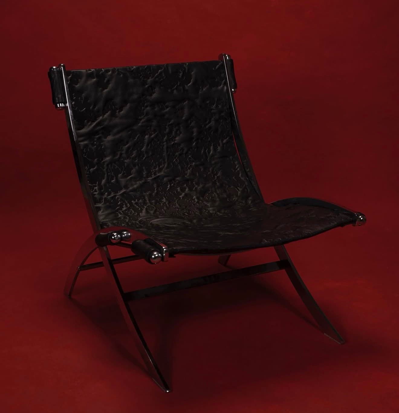 A modern lounge chair with a striking contemporary design. The chair features a polished chrome metal frame with a distinctive angular and curved structure, supporting a seat and backrest upholstered in black material with a textured, crinkled finish. The armrests consist of cylindrical black elements secured by chrome fixtures. — 3D model