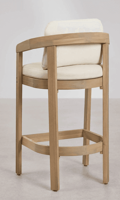 A wooden bar stool with a light wood finish. It features a rectangular seat and backrest, both upholstered in a cream-colored fabric. The stool has four legs connected by a circular footrest. The armrests are integrated into the frame, curving downwards from the backrest supports. — 3D model