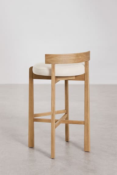 A modern bar stool featuring a light-toned oak wood frame and a circular cream upholstered seat. It has a low, gently curved backrest and a square-profile leg structure with an X-shaped cross-brace footrest. — 3D model