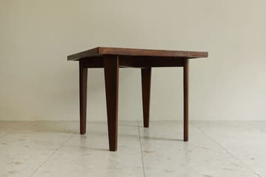 A square wooden table featuring a dark finish and four tapered legs, presented against a light-colored wall and tiled floor. — 3D model
