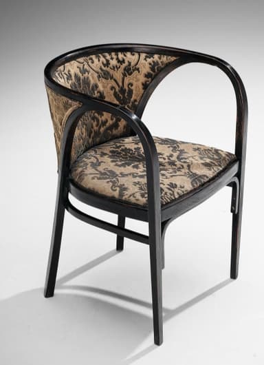 A dark-stained bentwood armchair featuring a distinctive barrel-back design. The frame is constructed from elegantly curved wood, forming integrated armrests and a supportive backrest. Both the seat and the inner backrest are upholstered in a patterned fabric, displaying a traditional damask or paisley motif in shades of dark brown/black and beige/gold. The chair stands on four straight legs, connected by simple stretchers for stability. The overall aesthetic suggests an early 20th-century or classic design. — 3D model