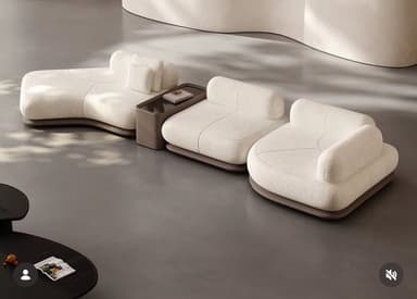 A modern modular sectional sofa system featuring a chaise lounge element, two armless seating modules, and an integrated rectangular side table. The sofa units are upholstered in a textured off-white bouclé-like fabric with soft, rounded forms and low-profile bases. The integrated table module has a dark brown finish and is positioned between two seating units, offering a functional surface. — 3D model