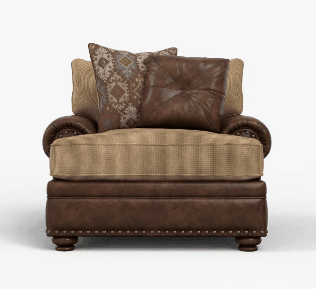 A traditional style accent chair featuring dark brown leather or faux leather upholstery on the frame, rolled arms, and base, complemented by a light beige ribbed fabric on the seat and back cushions. The chair is adorned with antique brass nailhead trim along the armrests and base. It comes with two decorative throw pillows, one in matching brown tufted leather and another with a geometric patterned fabric. The chair rests on short, turned wooden feet. — 3D model