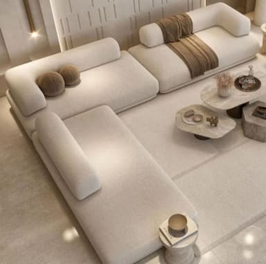 A modular sectional sofa with a low profile and rounded armrests. The sofa is upholstered in a textured light-colored fabric and features a configuration of multiple seating units that can be rearranged. It is accompanied by several decorative throw pillows and a draped throw blanket. The overall aesthetic is modern and minimalist. — 3D model