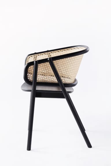 A modern armchair featuring a black finished solid wood frame, a natural cane woven backrest, and a light grey upholstered seat cushion. The chair has a sleek, minimalist design with integrated armrests that flow from the backrest. — 3D model