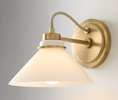 A contemporary wall sconce featuring a brushed brass finish on its mounting plate and arm. It has a white ceramic collar connecting the arm to a conical frosted glass shade, which diffuses light evenly. An exposed, fabric-wrapped electrical cord adds a subtle industrial touch. — 3D model