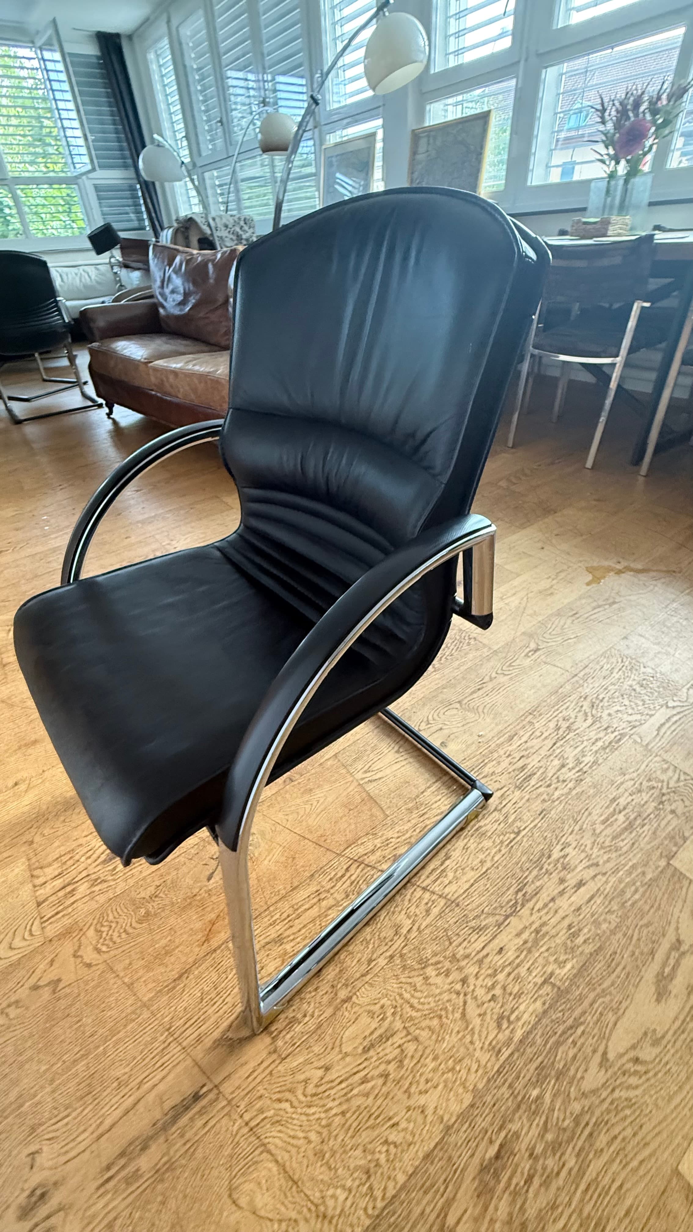 A modern black leather cantilever chair featuring a chrome frame and armrests, with padded seat and backrest. — 3D model