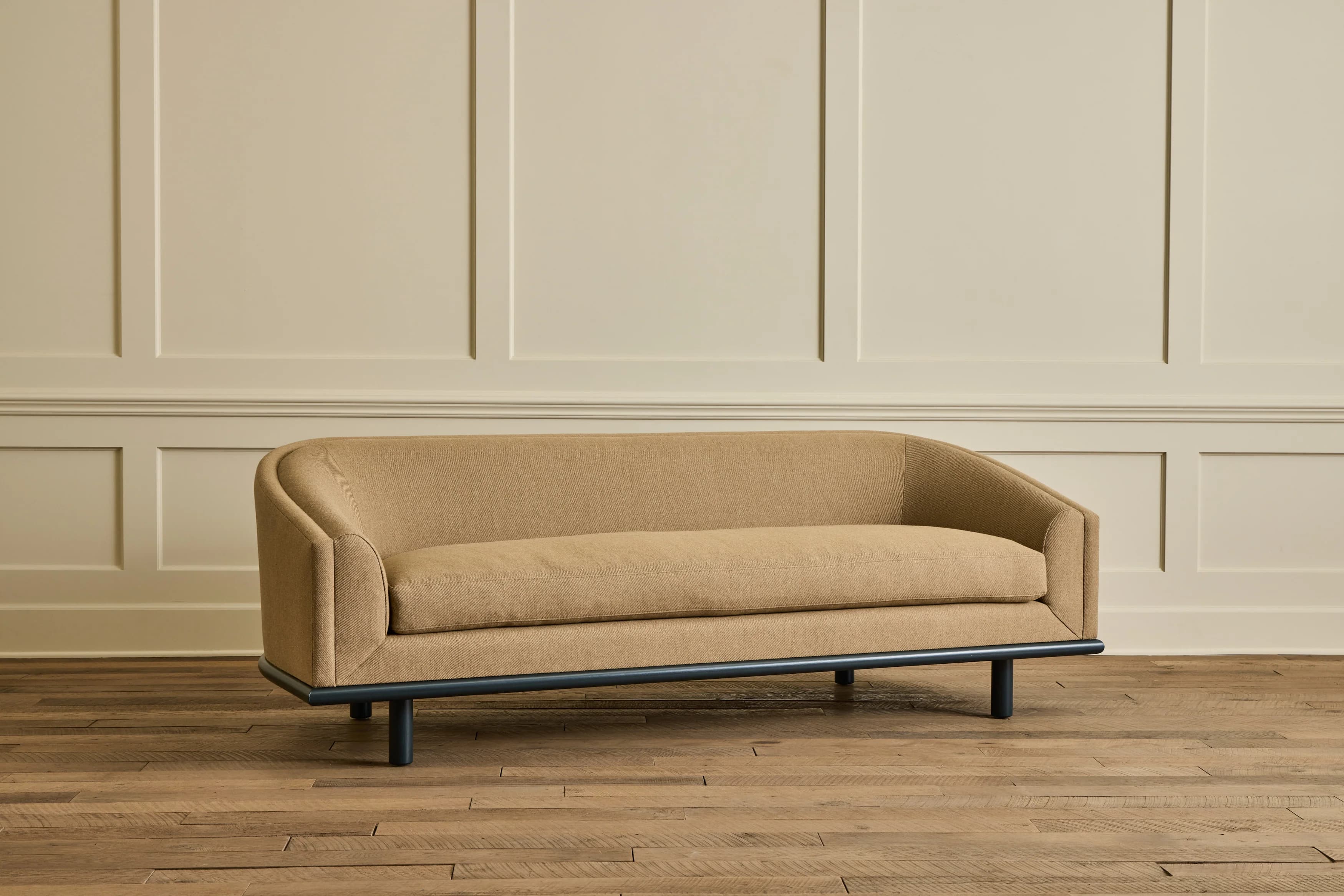 A contemporary sofa with a curved back and arms. The upholstery appears to be a textured fabric. The base is a dark, slender frame supported by four short, cylindrical legs. The overall design suggests a modern aesthetic. — 3D model