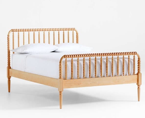 A wooden bed frame with a headboard and footboard featuring a spindle design. The frame has a light wood finish and is supported by four tapered legs. White bedding, including pillows and a sheet, is visible on the mattress. — 3D model