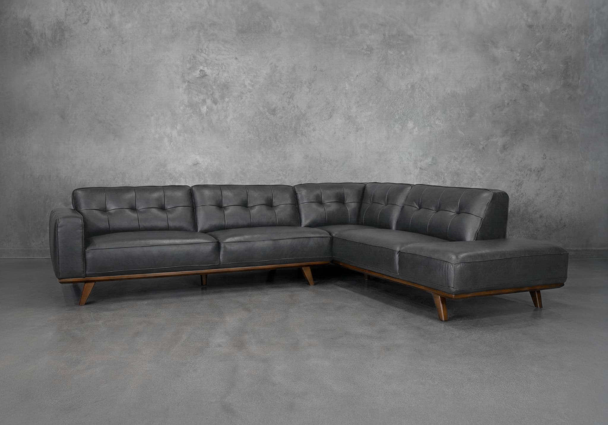 A dark grey sectional sofa with tufted back cushions and seating. The sofa has a low profile and is supported by angled wooden legs. The frame appears to be upholstered in leather or a similar material, with visible stitching and a sleek, modern design. — 3D model