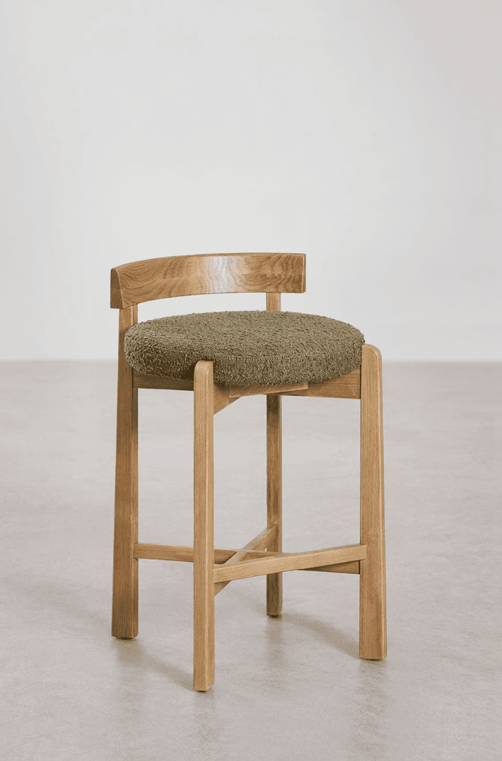 A modern counter stool featuring a light natural wood frame and a round upholstered seat in a textured olive green fabric, complemented by a low, curved wooden backrest. — 3D model