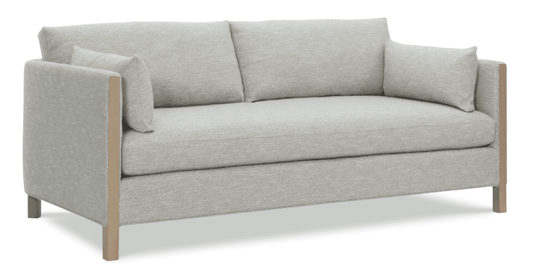 A two-seater sofa with a low profile and upholstered frame. It features two seat cushions and two back cushions, along with two smaller accent pillows. The arms and base are integrated into the overall design, with visible wooden framing elements on the outer sides of the arms and extending down to the legs. The upholstery appears to be a textured, woven fabric. — 3D model
