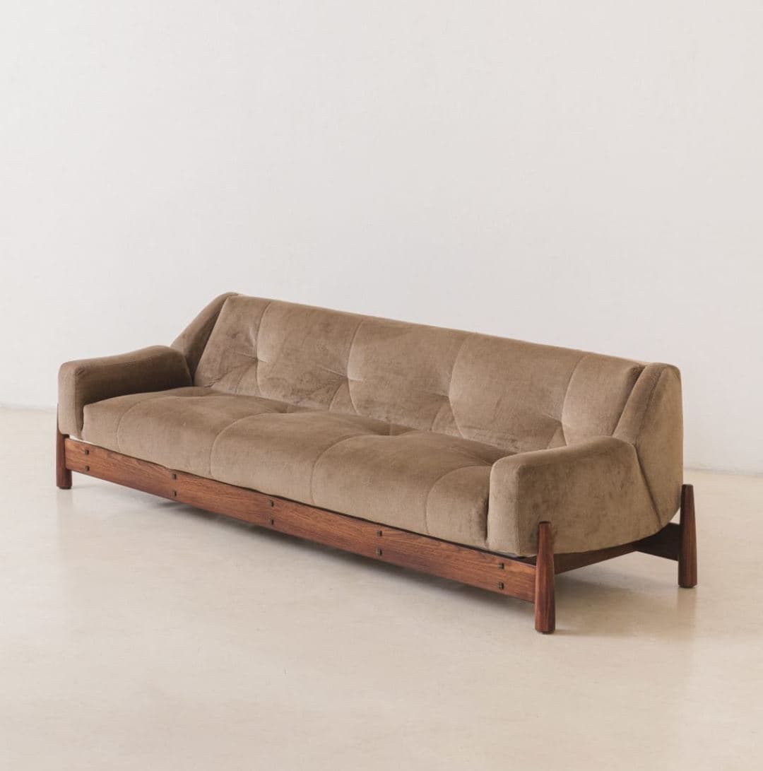 A mid-century modern style sofa with a tufted back and seat. It features a low-profile wooden base and armrests with rounded edges. The upholstery appears to be a soft, textured fabric in a neutral tone. — 3D model