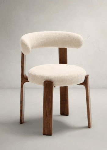 A modern upholstered armchair with a curved backrest and a circular seat. The frame and legs are constructed from dark wood with a visible grain, providing a contrast to the cream-colored fabric upholstery. The design is minimalist and contemporary. — 3D model