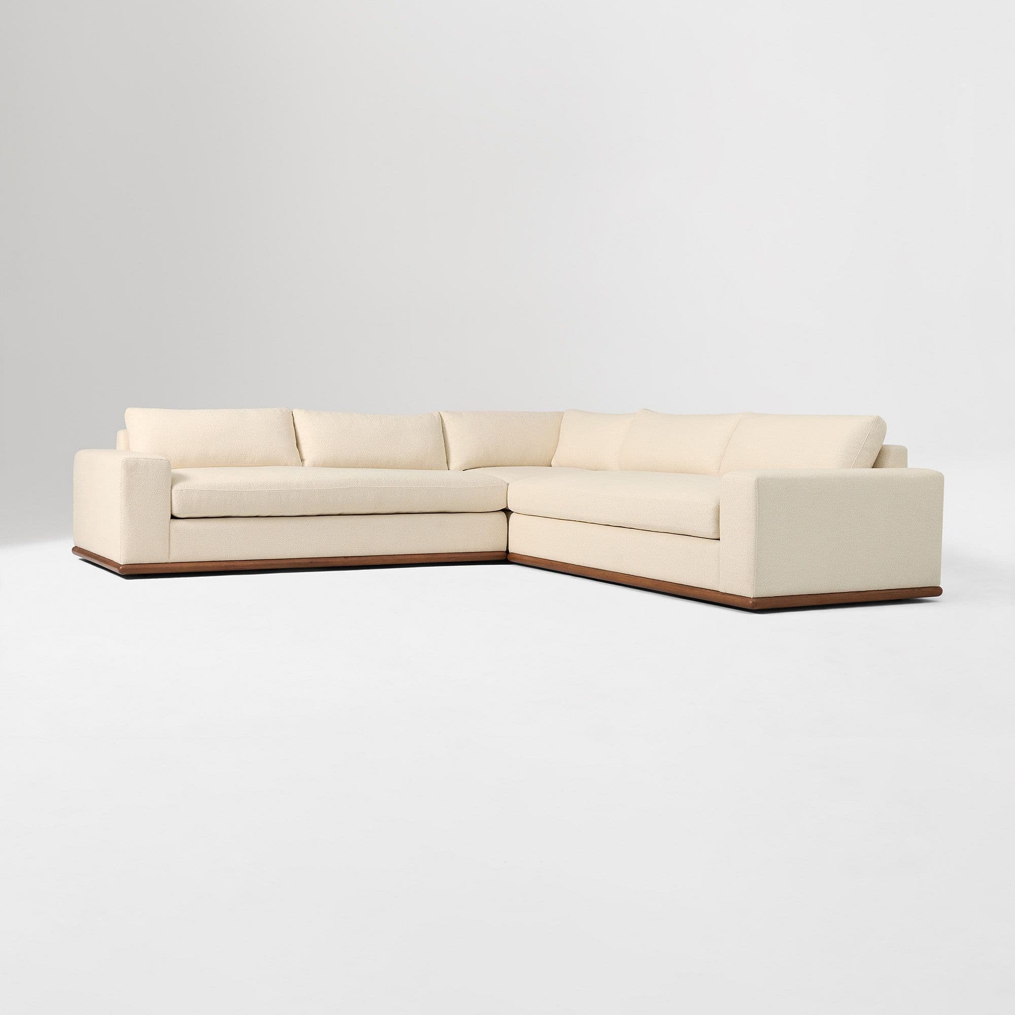 A large, L-shaped sectional sofa with a low profile and clean lines. The sofa features a fabric upholstery in a light, neutral tone and is supported by a dark, horizontal wood base that wraps around the perimeter. — 3D model