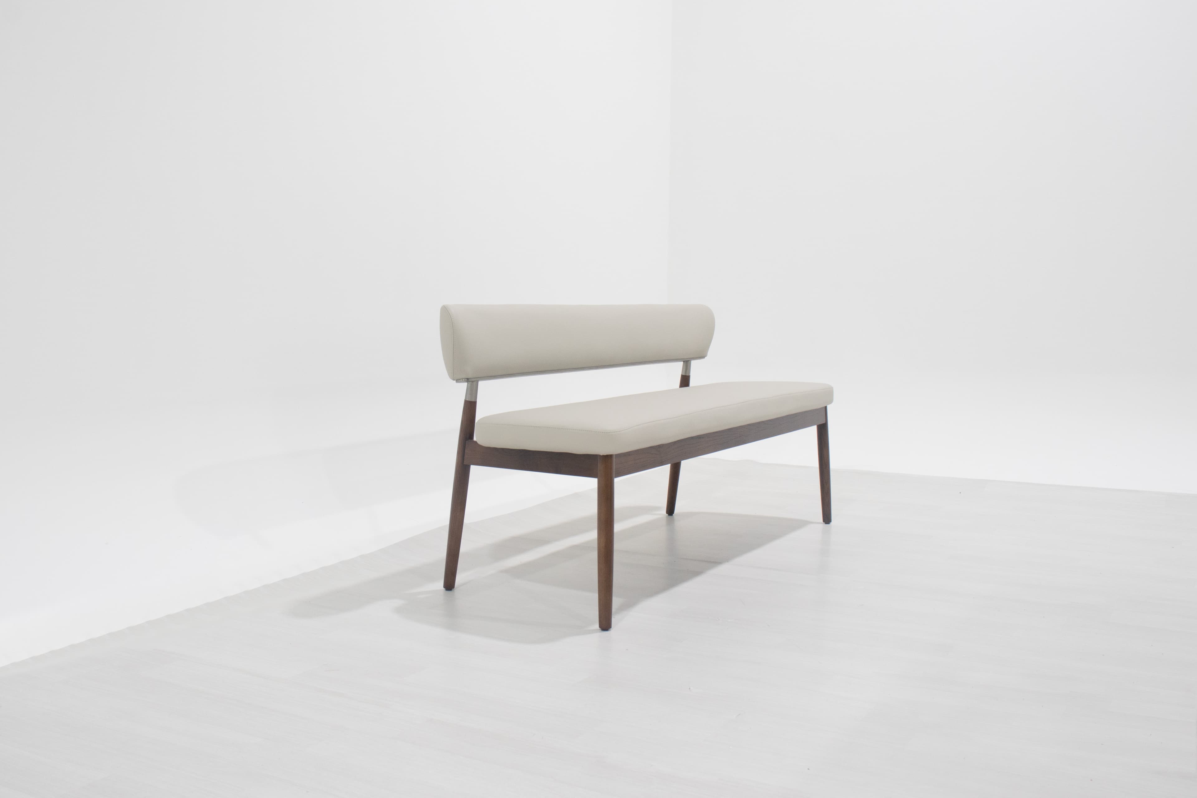 A modern upholstered bench featuring a dark brown wooden frame with tapered legs and a light beige or cream-colored upholstered seat and cylindrical backrest, supported by a metal bar. — 3D model