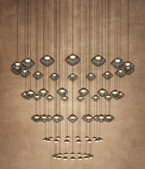 A sophisticated modern chandelier comprising numerous individual pendants arranged in a tiered, cascading formation. Each pendant features a unique geometric, faceted, or rhombus-shaped shade made of smoked or tinted glass, housing an integrated light source. The pendants are suspended at varying lengths by slender wires, creating a sculptural and dynamic lighting fixture. — 3D model
