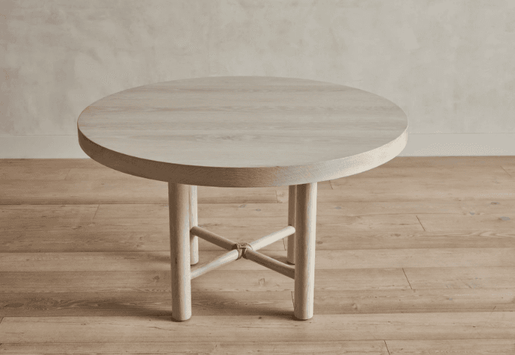 A round, light-colored wooden coffee table with a thick tabletop and four cylindrical legs. The legs are joined by a cross-brace structure, which is tied together in the center with what appears to be natural fiber rope. The wood grain is visible and has a slightly weathered or bleached appearance. — 3D model