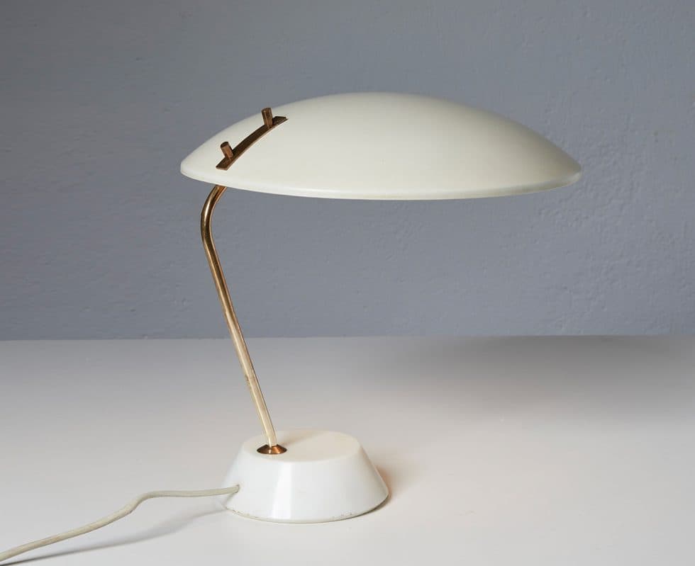 A mid-century modern table lamp with a creamy white, mushroom-shaped shade and a slender, curved brass stem. The base is a simple, conical white shape, and the lamp is connected to a power cord. Small brass accents secure the shade to the stem. — 3D model