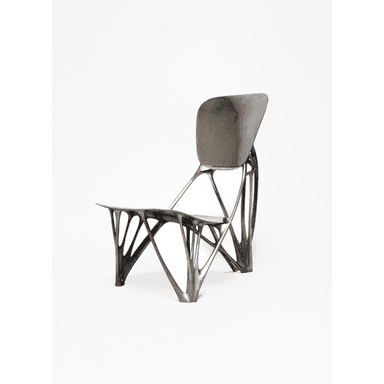 A contemporary chair featuring an intricate, dark-colored biomorphic skeletal base that supports a smoothly contoured, matte grey seat and backrest. The design is sculptural and avant-garde. — 3D model (AI enhanced source)
