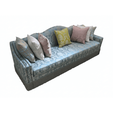 An elegant upholstered sofa featuring a light blue damask fabric with an ornate floral pattern. The sofa has a curved camelback design and rolled arms. A decorative fringe trim runs along the entire bottom edge, serving as a skirt. The seating area includes a single, long cushion, and the sofa is adorned with an assortment of throw pillows in complementary colors like pink, yellow, cream, and blue, all with various patterned fabrics. — 3D model (AI enhanced source)