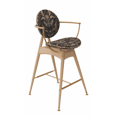 A tall, contemporary bar stool featuring a light-toned wooden frame, brass accents, and distinctive dark, patterned upholstery. The seat and backrest are circular and upholstered with a black fabric featuring an intricate floral and animal pattern in gold and bronze tones. The backrest is supported by curved brass elements that also form integrated armrests. The splayed wooden legs are reinforced by brass stretchers that serve as a footrest and terminate in brass caps. — 3D model (AI enhanced source)