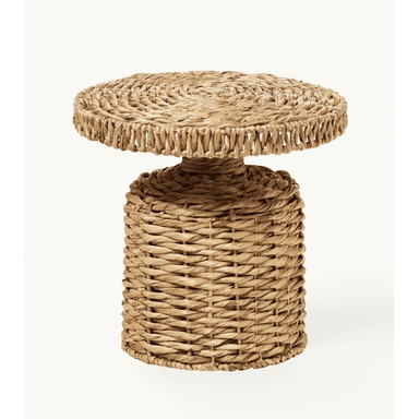 A small, round pedestal accent table crafted entirely from woven natural fibers, likely seagrass or water hyacinth. It features a solid cylindrical base that tapers slightly towards a smaller central column, which supports a thick, round tabletop. The weaving exhibits varying patterns, with a tighter, spiraled weave on the tabletop and a more open, basket-like weave on the cylindrical base. The table has a natural, earthy tone. — 3D model (AI enhanced source)