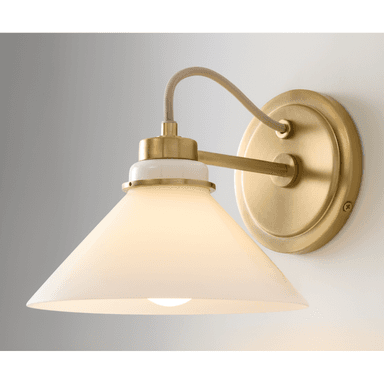 A contemporary wall sconce featuring a brushed brass finish on its mounting plate and arm. It has a white ceramic collar connecting the arm to a conical frosted glass shade, which diffuses light evenly. An exposed, fabric-wrapped electrical cord adds a subtle industrial touch. — 3D model (AI enhanced source)