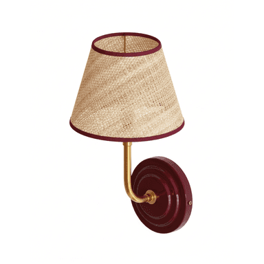 A wall lamp featuring a conical lampshade made of woven natural fibers, possibly straw or rattan, with a dark red trim along the top and bottom edges. The lampshade is supported by a curved, brass-colored metal arm extending from a circular wall mount. The wall mount is a deep red color with a subtle concentric ridged design. — 3D model (AI enhanced source)