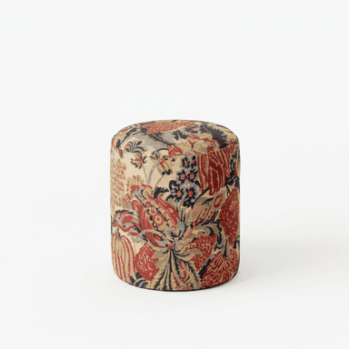 A cylindrical ottoman upholstered in a fabric with a detailed floral and botanical pattern. The pattern features large red and burgundy floral motifs interspersed with smaller dark blue and olive green elements against a light beige or cream background. The shape is a simple cylinder with a rounded top surface. — 3D model (AI enhanced source)