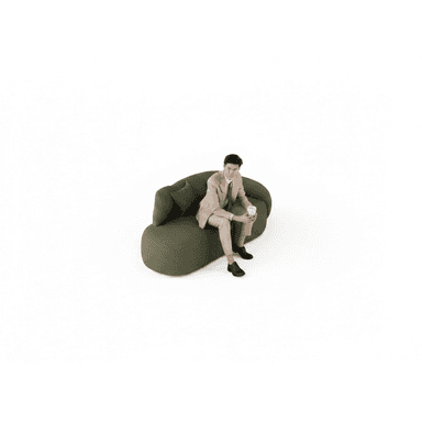 A modern, organically shaped sofa with rounded edges and a low profile. It is upholstered in a textured green fabric and features a single integrated armrest/backrest that curves around to form a partial enclosure. A single loose cushion is placed on the sofa. A man in a suit is seated on the right side of the sofa, holding a paper cup. — 3D model (AI enhanced source)