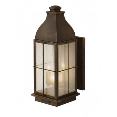 A traditional-style outdoor wall-mounted lantern light fixture. It features a rectangular body with a sloped, peaked roof and a finial at the top. The frame is made of aged bronze-finish metal, enclosing textured, seeded glass panels. Two internal light sources, resembling candelabra bulbs, are visible, casting a warm glow. The fixture has a decorative base designed for secure wall mounting. — 3D model (AI enhanced source)